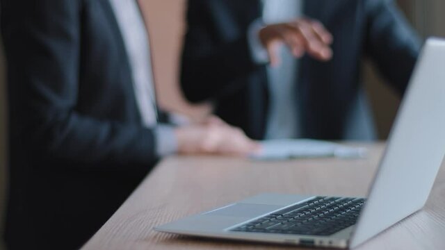 Close-up of modern laptop computer stands on table in office against background of two blurred business men in formal suits discussing about documents paper negotiating brainstorm discussing gesturing