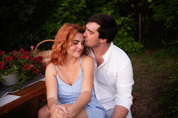 Fototapeta premium A young brunette man gently kisses a beautiful red-haired girl on the forehead, she laughs. Close-up portrait of couple in love, resting on picnic at trailer truck. Lovers kiss, hug. Travel honeymoon