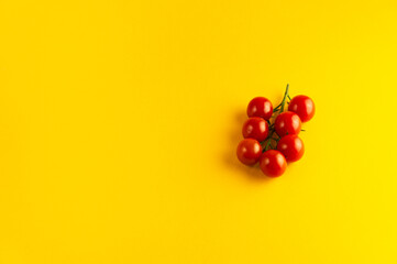 A sprig of cherry tomatoes on a bright yellow background with an empty place for an inscription.