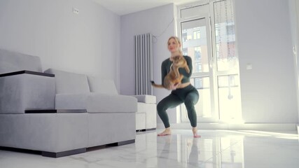 young fitness woman in sportswear performs squat exercises together with her pet in one at home in the living room. Woman workout and. physical exercise with along with a funny cat. Warm floor