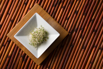 Alfalfa sprouts in a square white dish on bamboo