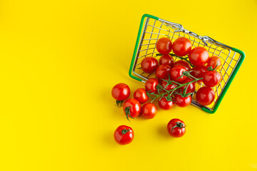 Scattered cherry tomatoes in a basket on a bright yellow background with an empty place for an inscription.