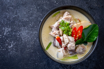 Chicken tom kha put in black bowl on wooden table and seasoning.