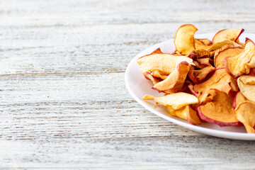A pile of dried apples in slices on a white plate on wooden background. Dried fruit chips. Healthy food