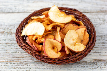 A pile of dried slices of apples in wicker basket on white wooden background. Dried fruit chips. Healthy food