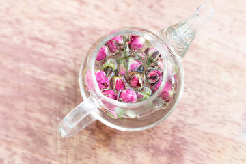 Close-up of a small teapot with rose tea on a wooden stand. Photo in bed colors, a gentle start to the day, a healthy morning drink for women from rosebuds, selective focus.