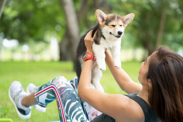 A healthy woman playing with a smiling corgi puppy while excersing on yoga mat, outdoor training...