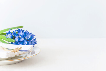 Beautiful place setting with white plates, golden fork and knife on white napkin and blue hyacinth on whit background. Close up, space for text