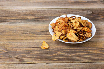 A pile of dried pears in slices on a white plate on wooden background. Dried fruit chips. Healthy food