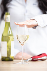 Female holding a hand above the glass of white wine with bottle and wine opener next to it
