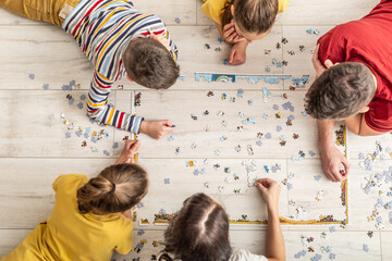 Top view of a family assembling puzzle on the floor at home