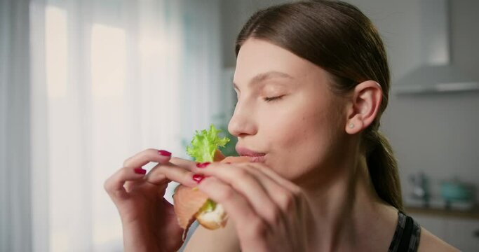 Zoom in shot of attractive young woman snacking on sandwich closing eyes from satisfaction. Healthy eating concept.
