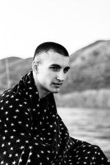 portrait of a beautiful young man in a plaid with five-pointed stars, in summer on the background of the sea coast black and white photo