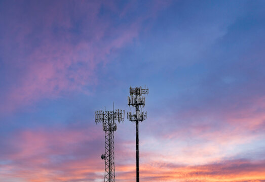 Two towers providing cellular broadband and data service to rural areas against the sunset. Illustrates digital divide.
