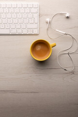 Smart working concept. Break time. Top view of a white wooden table with  a cup of coffee, computer keyboard and earphones on it. Copy space for text.