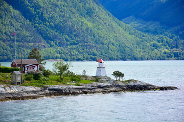 Small lighthouse stands on a promontory in a fjord with a traditional wooden house in the Lofoten...