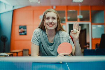 Portrait of a smiling teen girl table tennis player with a ping pong racket. Waving hand
