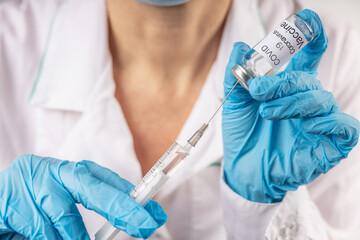 Vial withCOVID-19 vaccine and a syringe with a needle for injections for coronavirus infection in the hand of a doctor in a nitrile glove on a white background. Close-up. Concept fighting Coronavirus