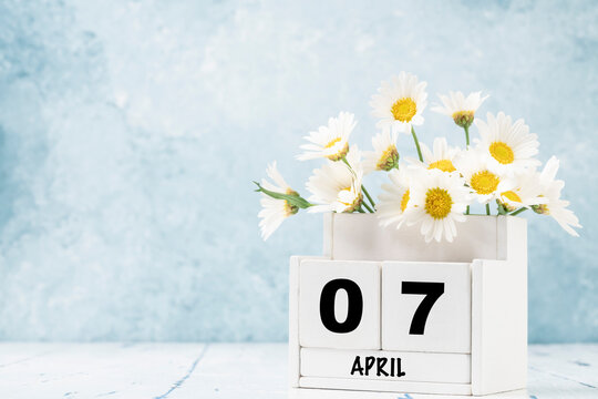 cube calendar for april decorated with daisy flowers over blue with copy space