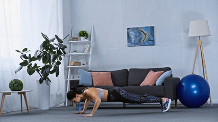 young woman in sportswear doing plank exercise at home