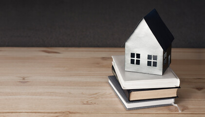 Obraz na płótnie Canvas Miniature paper mock-up of a house on a book. Concept of mortgage, rent, purchase, protection, construction of a house. On a wooden background