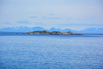 small stone island in the sea in Lofoten in Norway with mountain range in the background