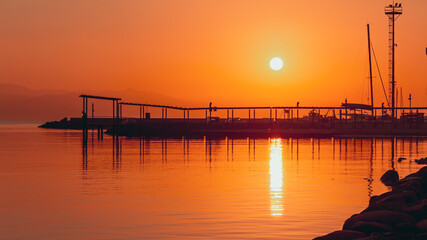 Fototapeta na wymiar Silhouette sunrise over the dock of Marina Piccola, soft waves and boat