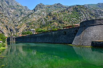 Fototapeta na wymiar Kotor, city walls with water-filled moat around the old town, with mountains in the background, Kotor, Montenegro