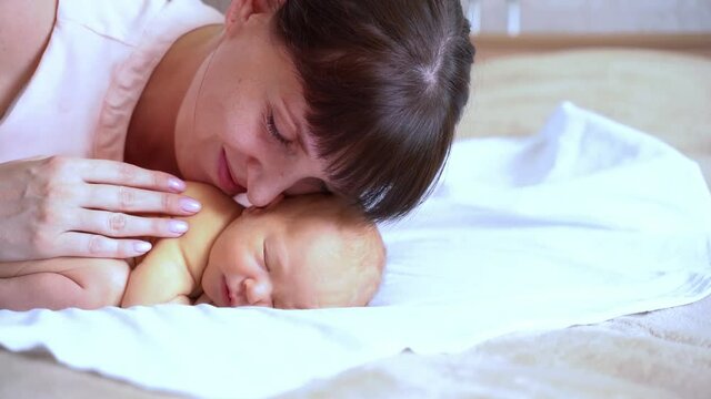 Little newborn child. Home family portrait. Mother kiss small son. Happy emotion. Lying in bed. Calm infant
