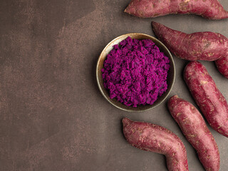 Purple yams pile and mashed potatoes on dish placed on a dark brown background with copy space for text. Purple sweet potatoes. Top view. Vegan fruit and healthy fruits concept