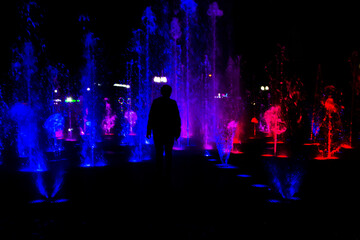Obraz premium Black Silhouette of a woman against the backdrop of a fountain backlit in blue