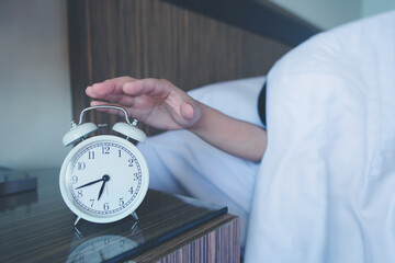Close up of man lying in bed turning off hand reaching out for alarm clock color black Wake up late...