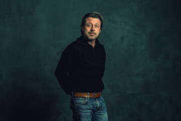 Man with stubble beard in black woolen sweater against grey wall