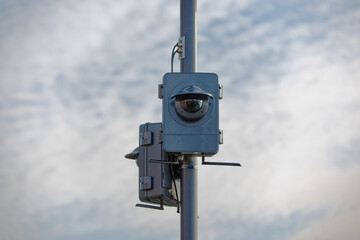 two large surveillance cameras on a light pole in cloudy sky with clouds in the background, dimmed light, during the day without people,