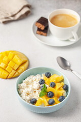 Cottage cheese with mango pieces and blueberries in a bowl on the table. Healthy breakfast