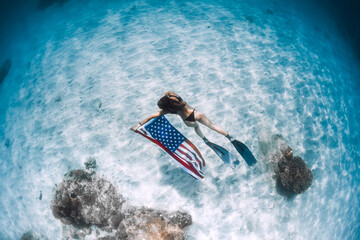 Freediver glides over sandy sea bottom with United States flag. Independence day
