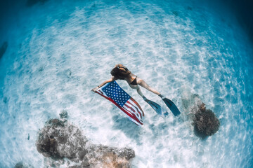 Freediver glides over sandy sea bottom with United States flag. Independence day
