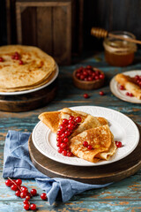 Pancakes with honey and red currants on white plate. Maslenitsa