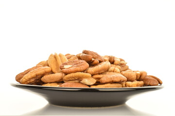 Fototapeta premium Several light brown organic shelled pecans in a black ceramic saucer, close-up, isolated on white.