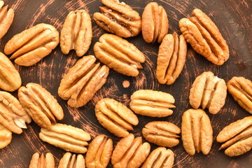 Several light brown organic shelled pecans in a clay plate, close-up, top view.