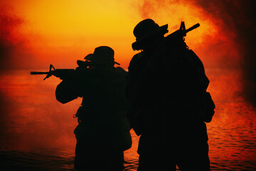 Commando soldiers walking in water, army special operations forces fighters sneaking in darkness, aiming assault rifles and observing shore during amphibious operation on coast at night or dawn