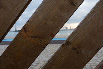 View of the seaport through the planks. Straight lines in perspective, evening landscape on the water and pier