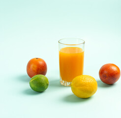 Juice in a tall glass surrounded by fruits. Blue background.