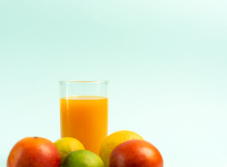 A glass of orange juice, fruits in the foreground. Blue background.