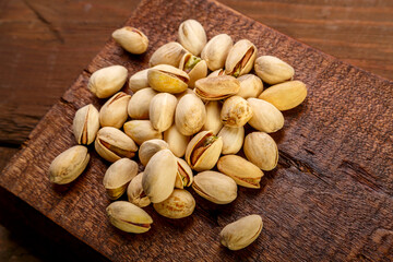 Pistachio nuts scattered on a square board on a wooden table.