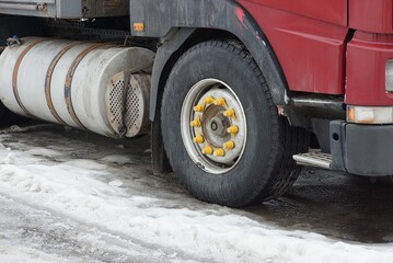 black front wheel on red truck with gray metal gas tank on white snow on winter street
