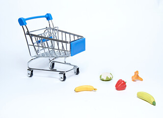 A blue supermarket grocery cart on an isolated white background with scattered fruits and vegetables.