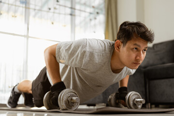 Fototapeta na wymiar Sport man doing strength training exercise pushup with dumbbell at home.