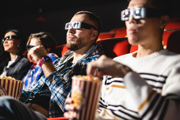 Friends watching a movie in the cinema with popcorn. People sit in the armchairs of the cinema and look at the screen with special glasses for 3D