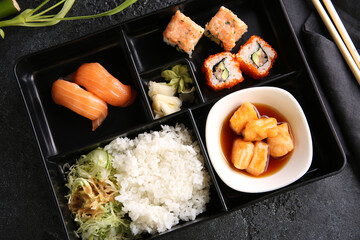 Japanese cuisine. Business lunch in a black box: rice, rolls, salad, sushi on a black table. Background image, copy space